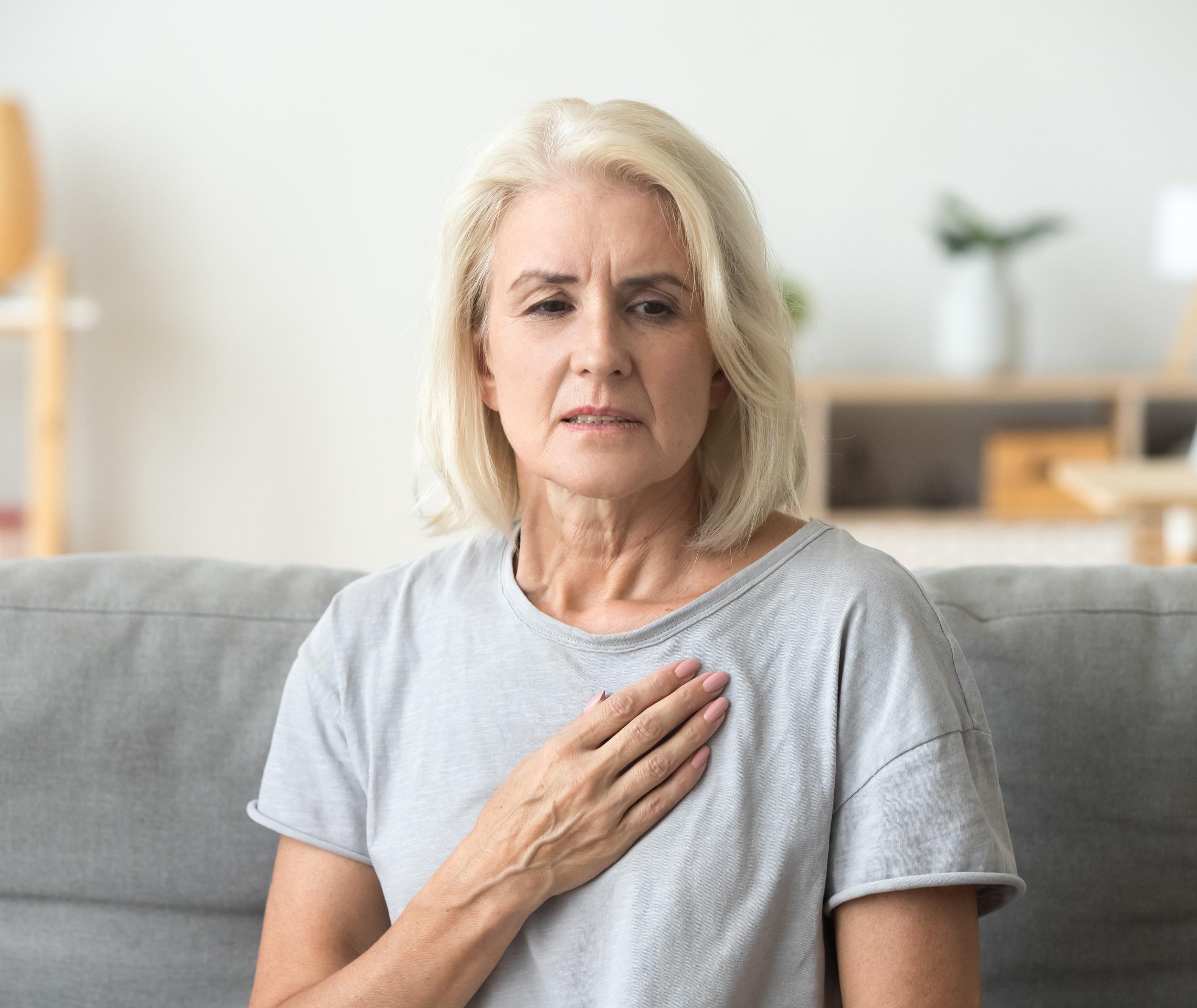 Als Symptom der Koronaren Herzerkrankung verspürt eine Frau Brustenge und fasst sich ans Herz.