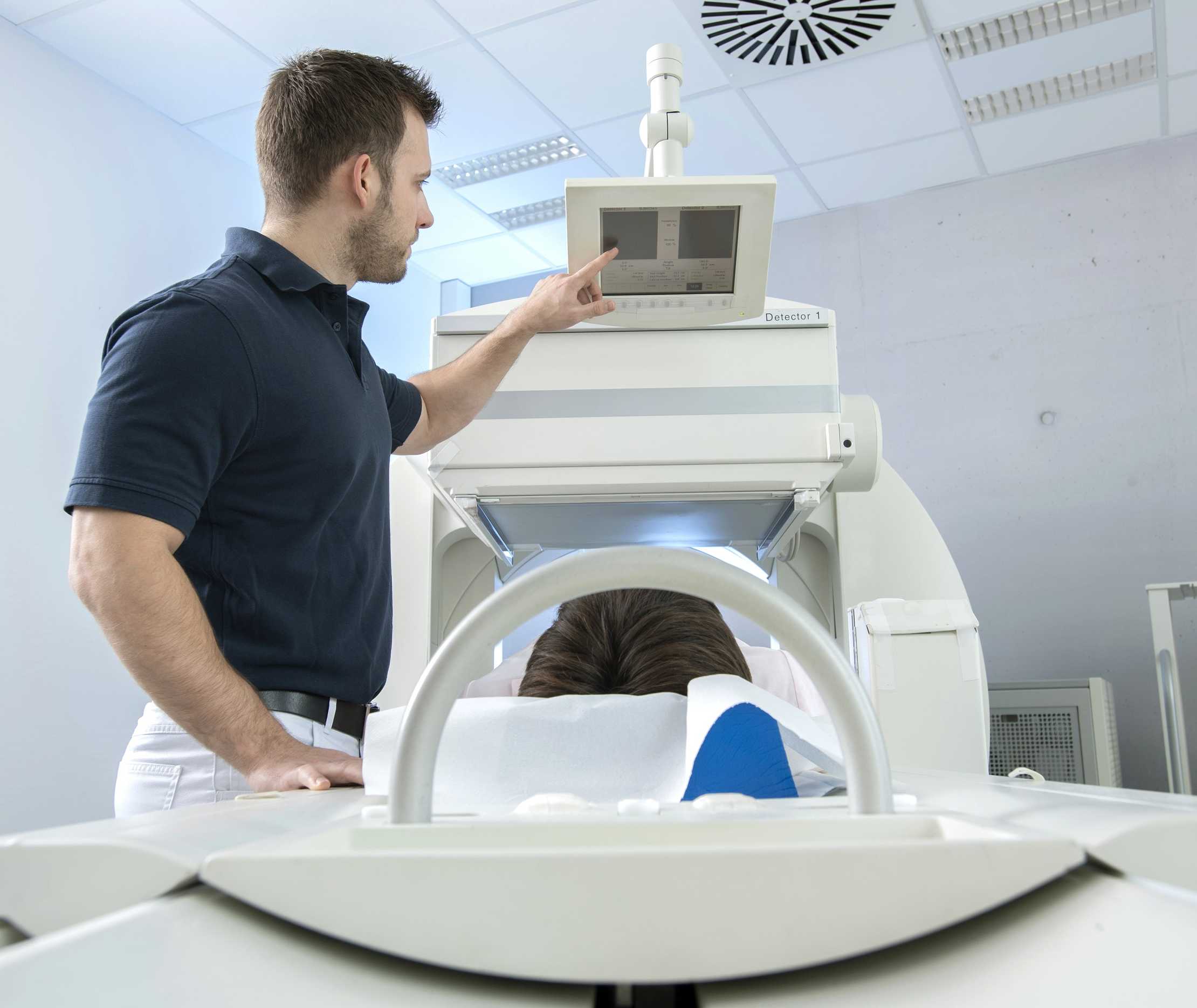 Medizinischer Fachangestellter fährt Patienten für eine Myokardszintigrafie in die Röhre.