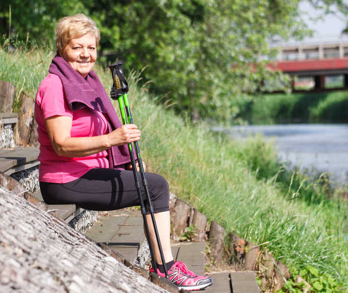 Eine Patientin mit Herzschwäche macht Rast in der Natur und hält zwei Nordic-Walking-Stöcke in der Hand.