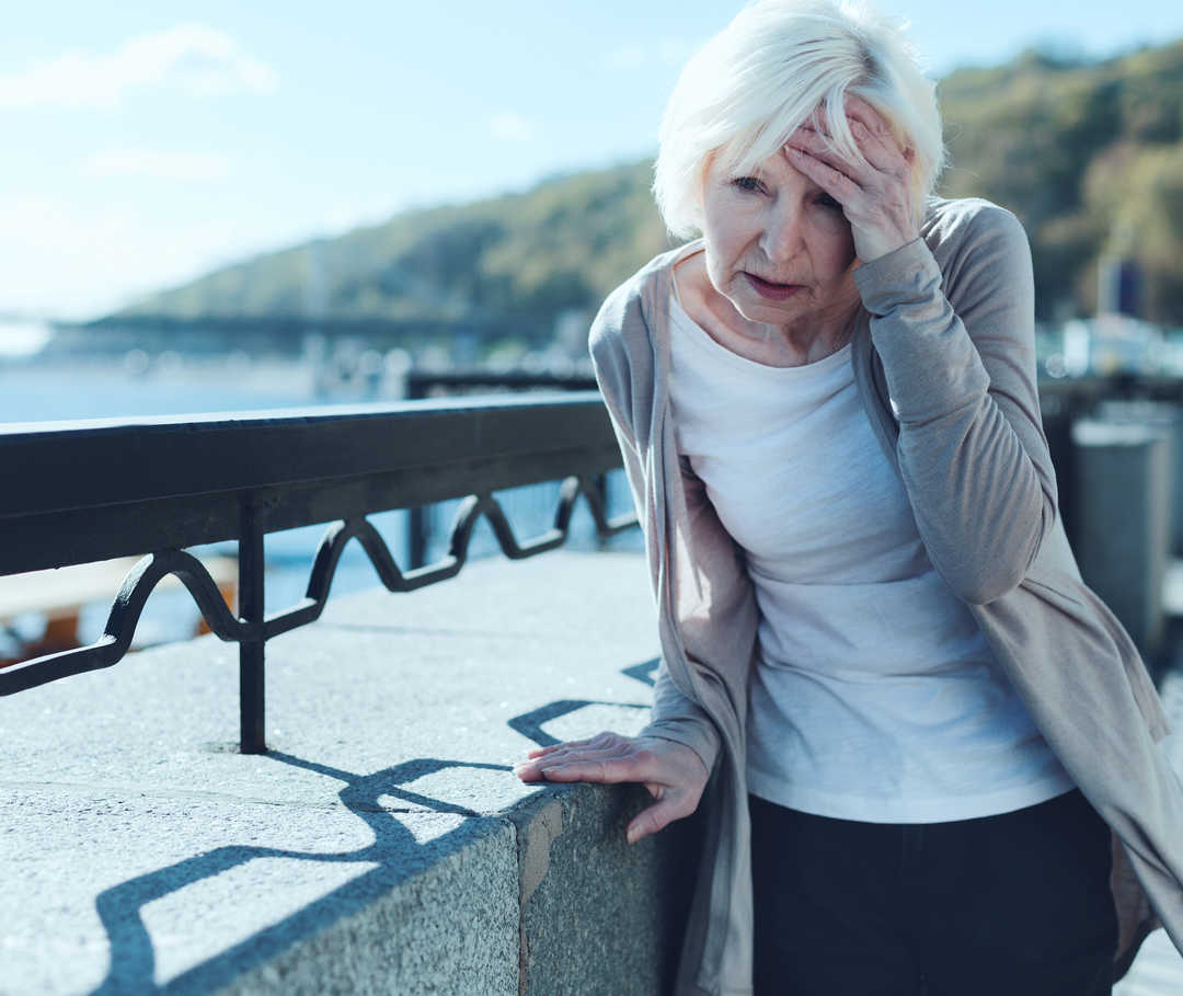 Eine Frau hält sich mit einer Hand an den Kopf und mit der anderen an einer Mauer fest.