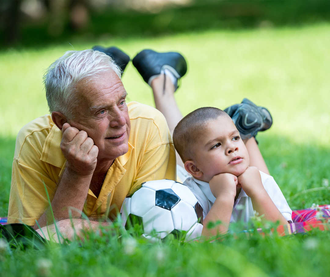 Chronische Herzinsuffizienz beeinträchtigt die Leistungsfähigkeit: Opa liegt mit Enkelsohn auf der Wiese.