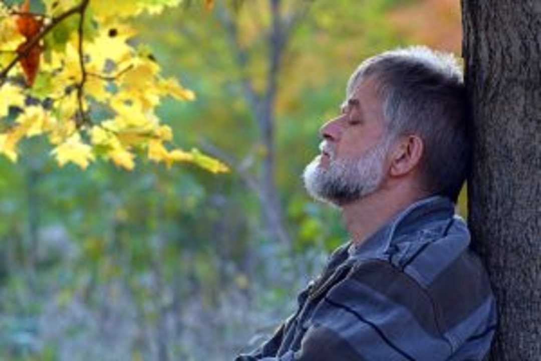 Mann lehnt an einem Baum, da er an globaler Herzinsuffizienz leidet.