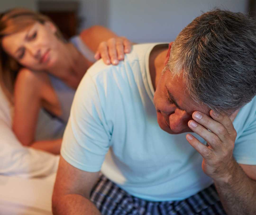 Mann mit Schlafapnoe sitzt auf Bettkante und stützt sich den Kopf.
