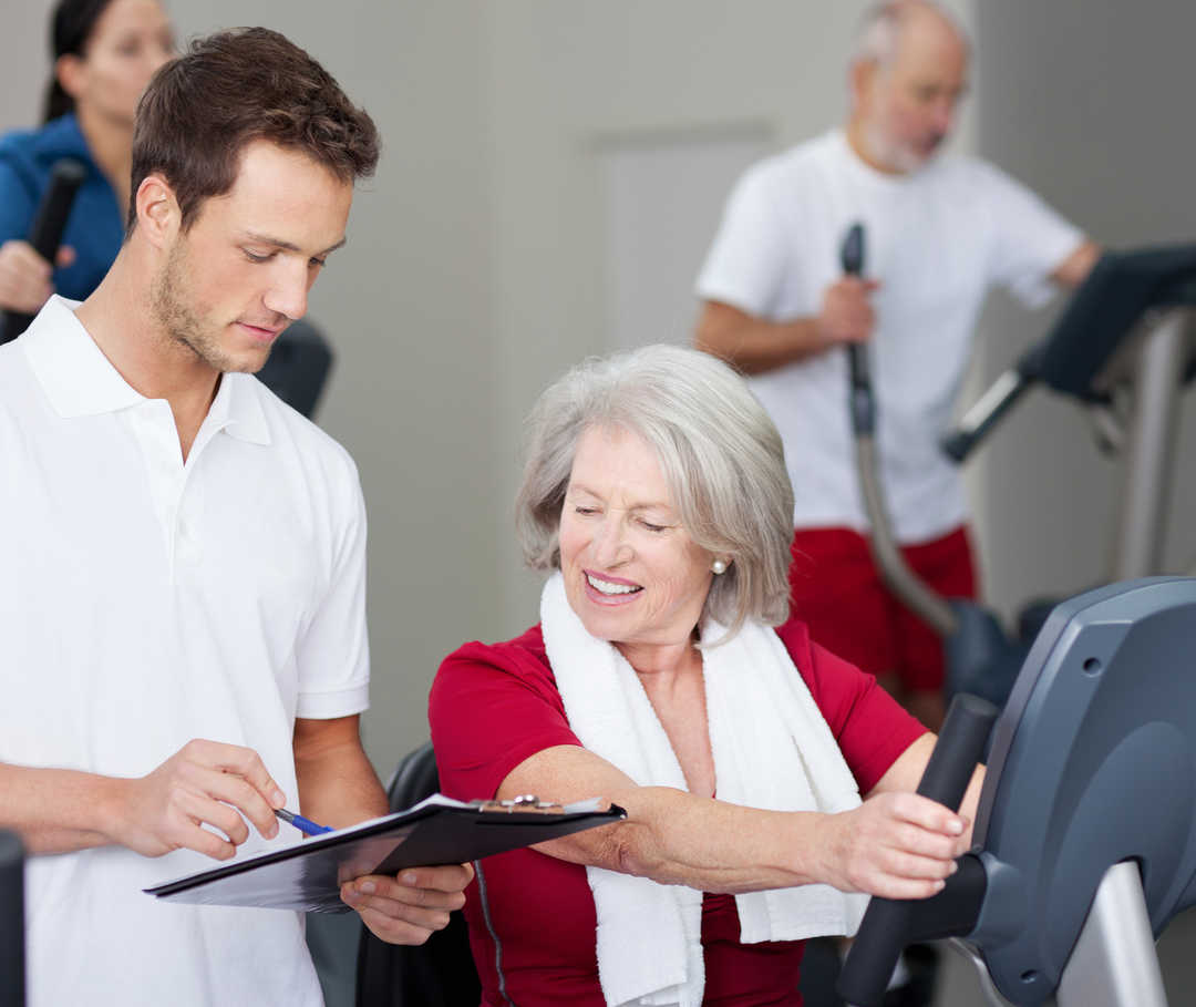 Training kann bei einer Herzschwäche die Belastbarkeit bessern. Fitnesstrainer erklärt Frau mit Herzschwäche ihren Trainingsplan.