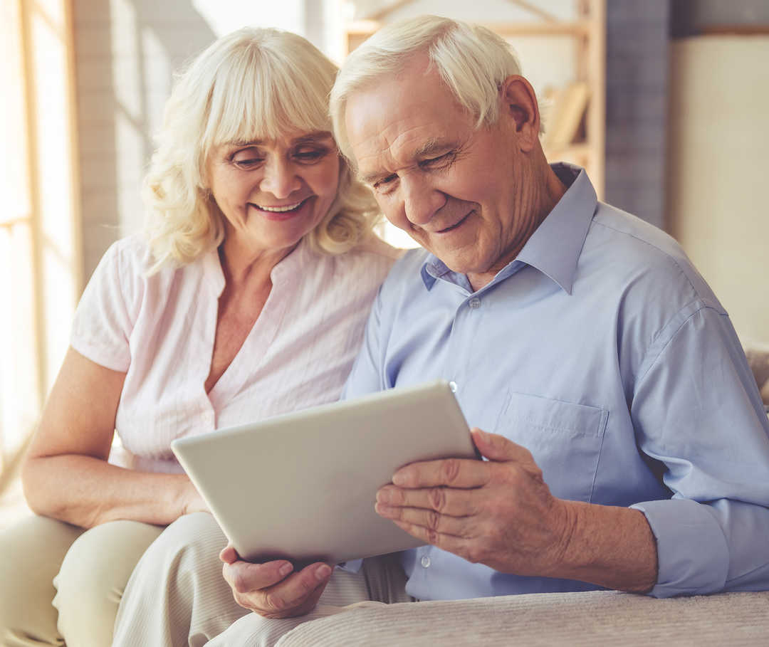 Ein Mann und eine Frau sitzen auf einem Sofa und blicken auf ein Tablet.