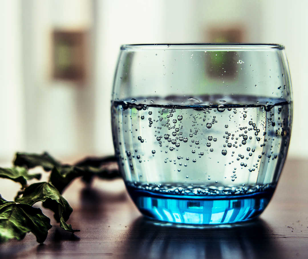 Glas Wasser am Tisch: Eine herzgesunde Ernährung beinhaltet eine angemessene Trinkmenge am Tag.