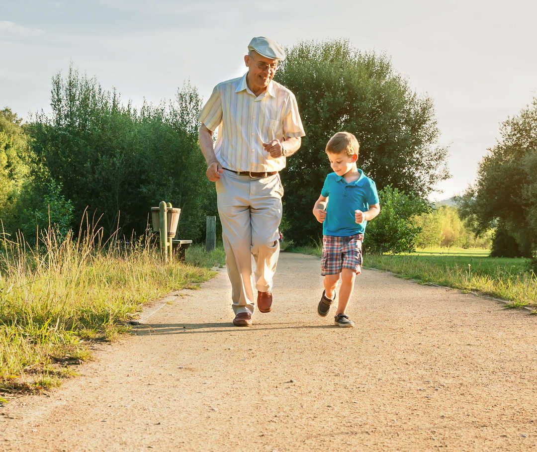 Herzinsuffizienz-Behandlung: Älterer Mann rennt mit Enkel einen Weg entlang.