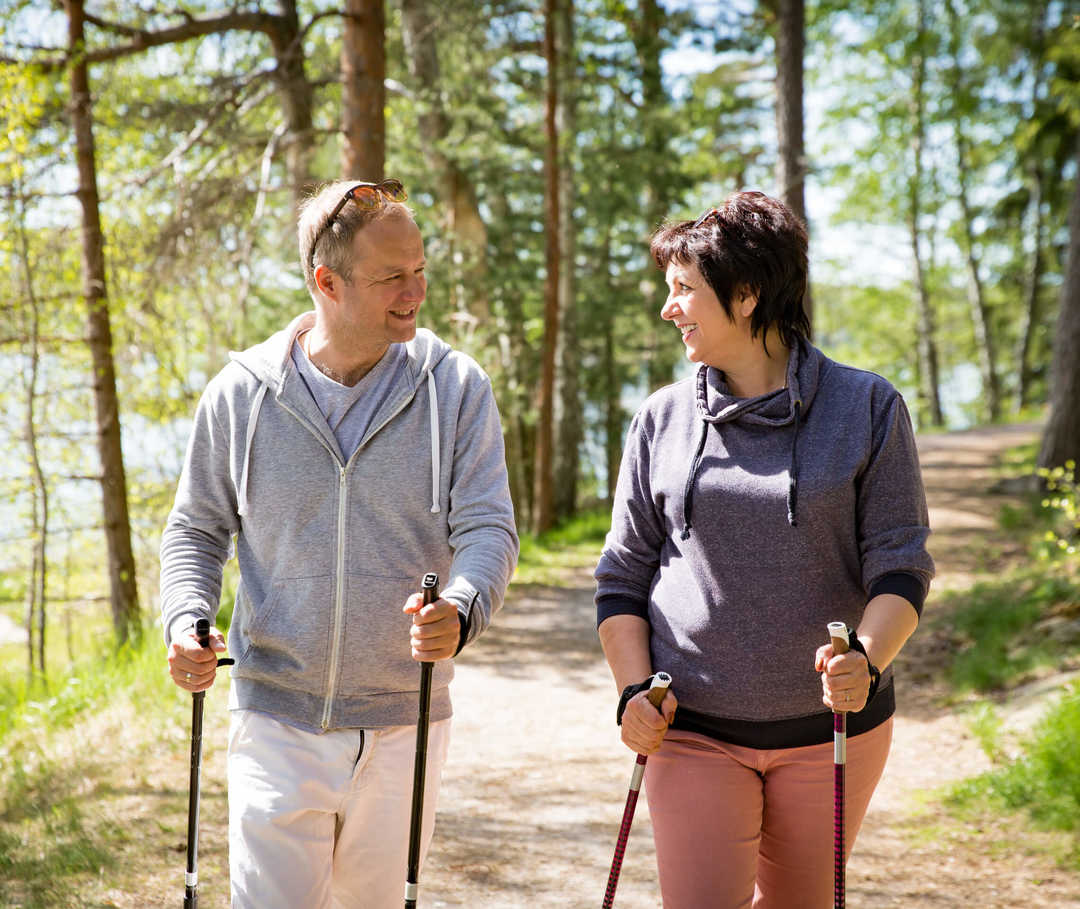 Mann und Frau im Wald beim Nordic-Walking: eine mögliche Behandlungsmaßnahme bei Bluthochdruck (Hypertonie).