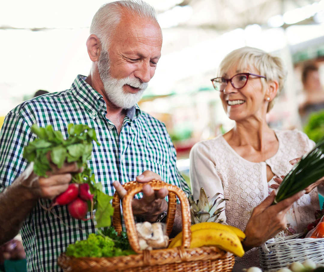 Bei Diabetes und Herzschwäche ist eine gesunde Ernährung wichtig. Diabetes und Herzinsuffizienz: Paar trägt Körbe mit frischem Gemüse vom Markt.