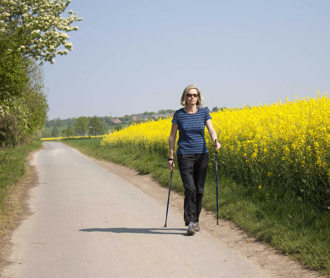 Eine Linksherzinsuffizienz kann bei Anstrengung zu Atemnot führen. Linksherzinsuffizienz: Frau beim Walken neben einem Rapsfeld.