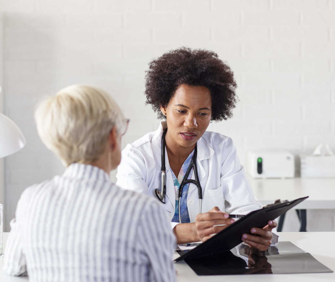 Herzinsuffizienz-Patientin sitzt mit Ärztin an einem Tisch und bespricht die richtige Einnahme von Betablockern.