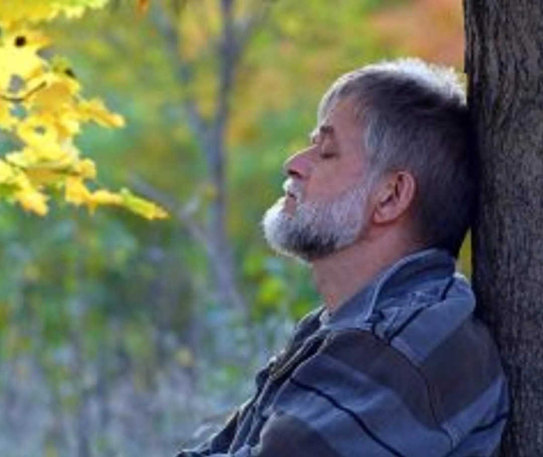 Mann lehnt an einem Baum, da er an globaler Herzinsuffizienz leidet.