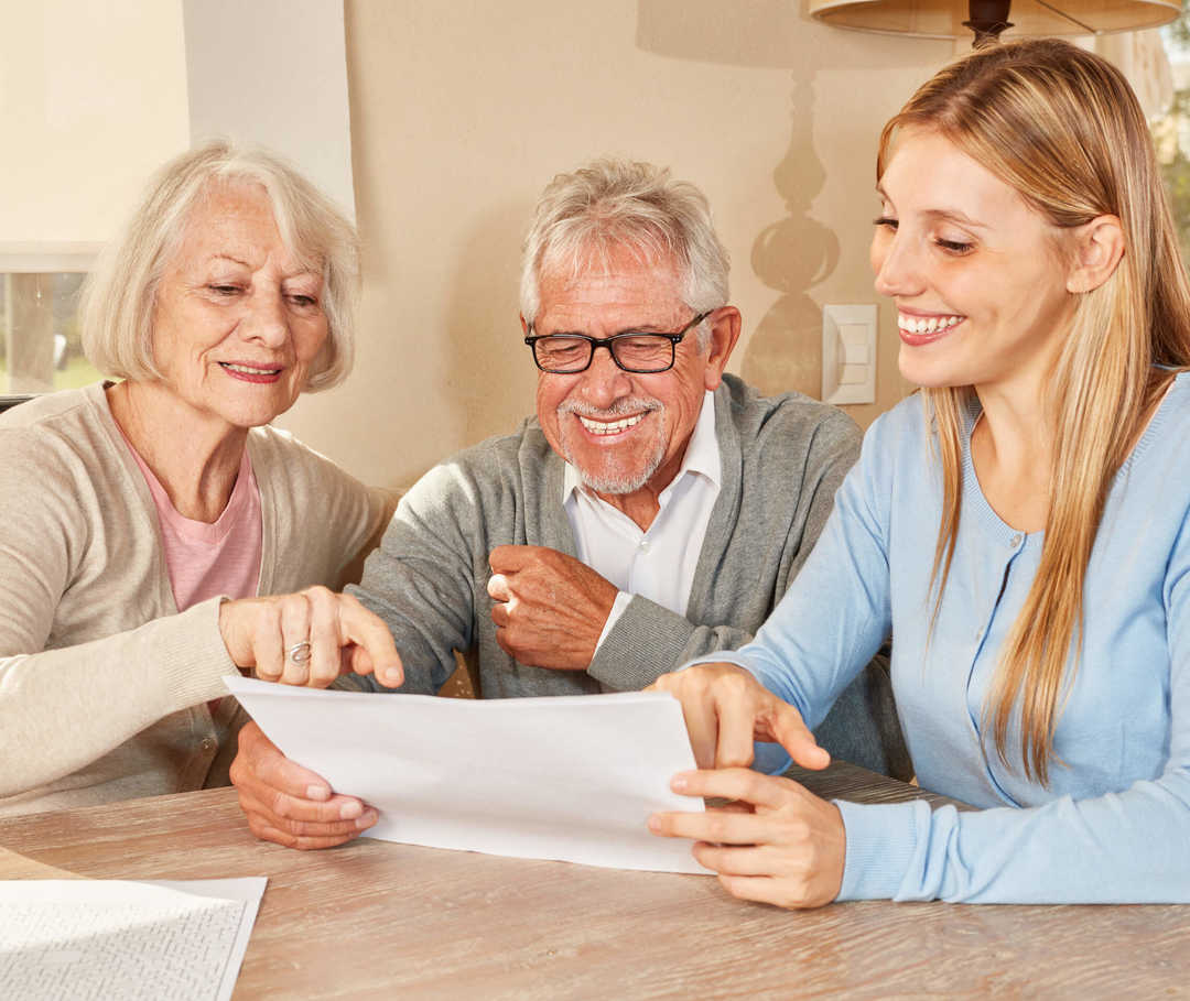 Tochter sitzt mit Mutter, die an Herzinsuffizienz leidet, und Vater am Esstisch und bespricht mit ihnen gemeinsam die Pflege.
