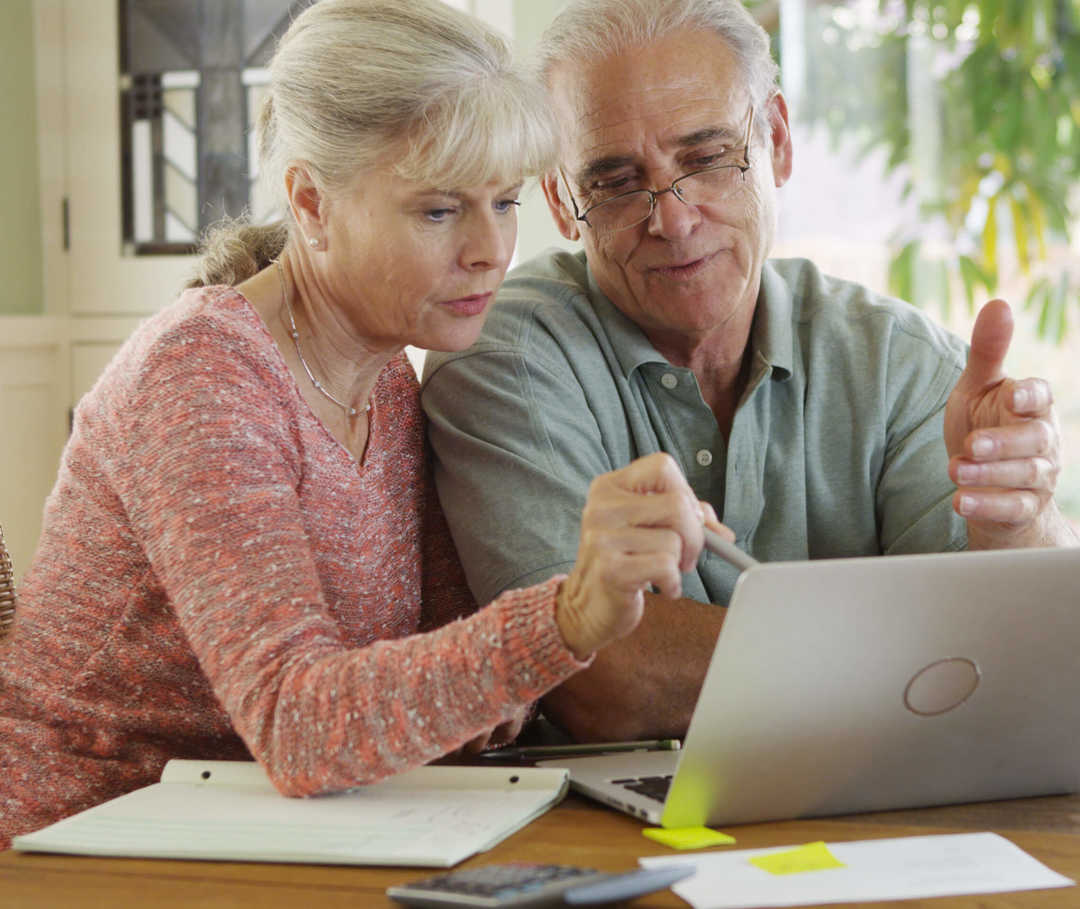 Eine Frau und ein Mann sitzen vor einem Laptop am Tisch.