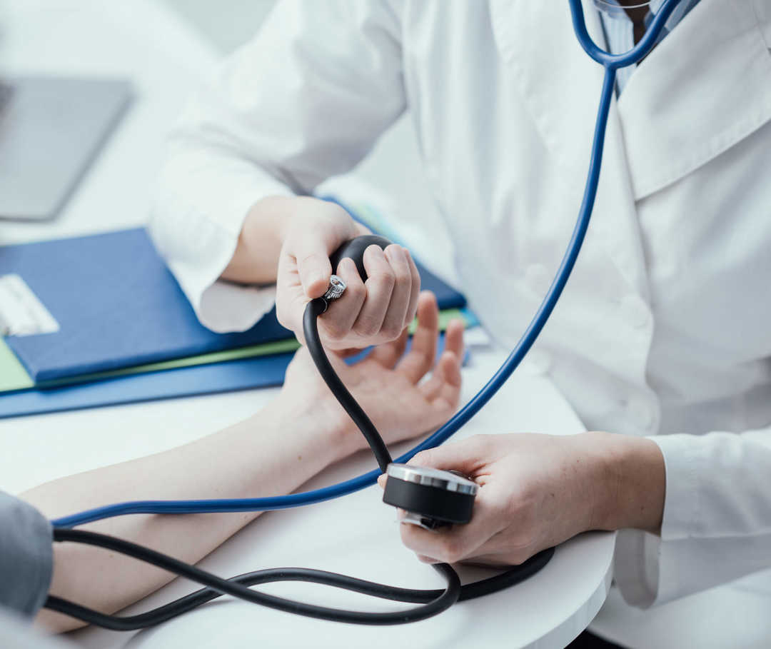 Eine Person in weißem Kittel misst den Blutdruck einer weiteren Person.