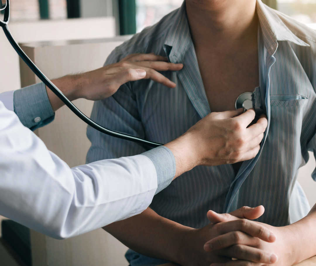 Ein Arzt hört Herz eines Mannes mit Stethoskop ab, um eine Herzbeutelentzündung zu untersuchen.