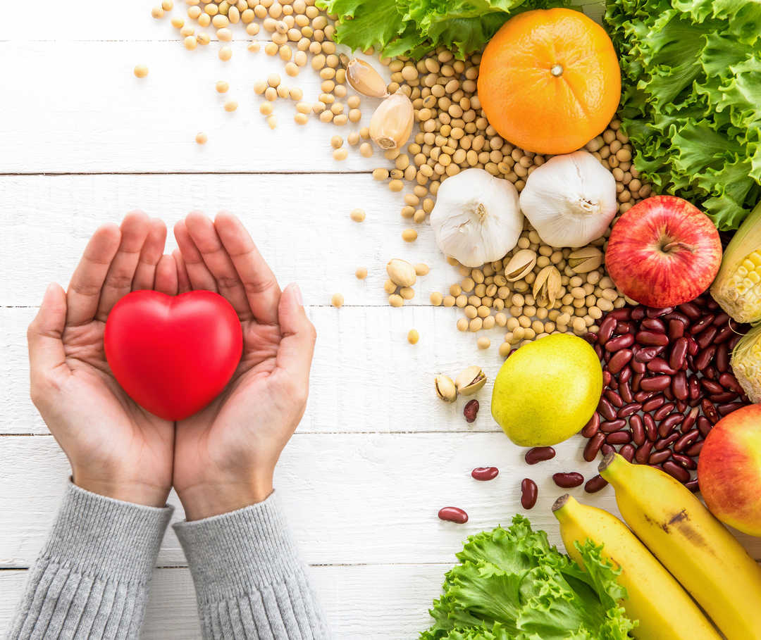 Eine gesunde Ernährung kann bei einer Hypercholesterinämie helfen. Hypercholesterinämie: gesunde Lebensmittel neben einem Herz