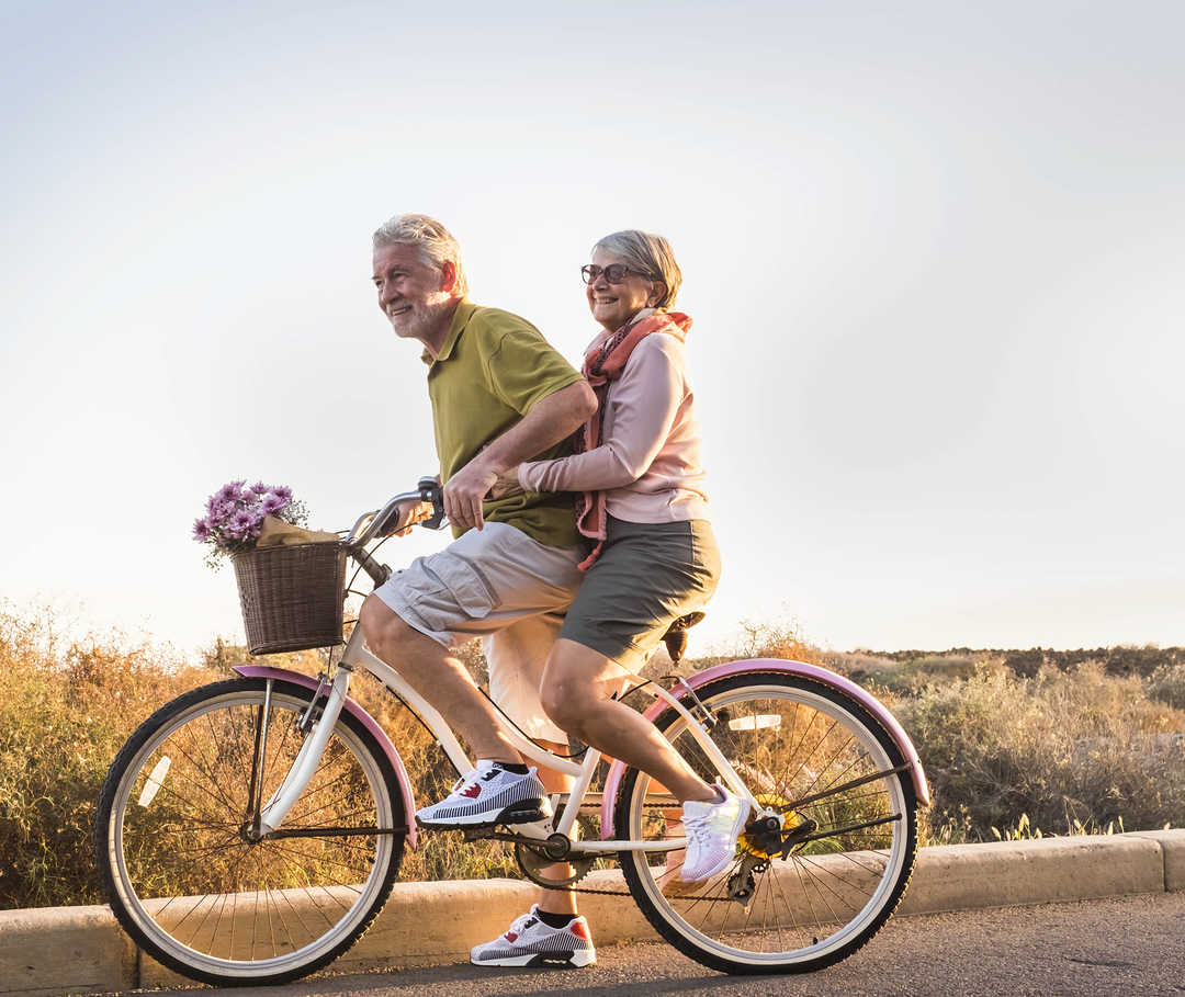 Mit Bewegung lässt sich das LDL-Cholesterin senken. Bild zeigt älteres Paar, das gemeinsam Fahrrad fährt – das ist auch gut für die Herzgesundheit.