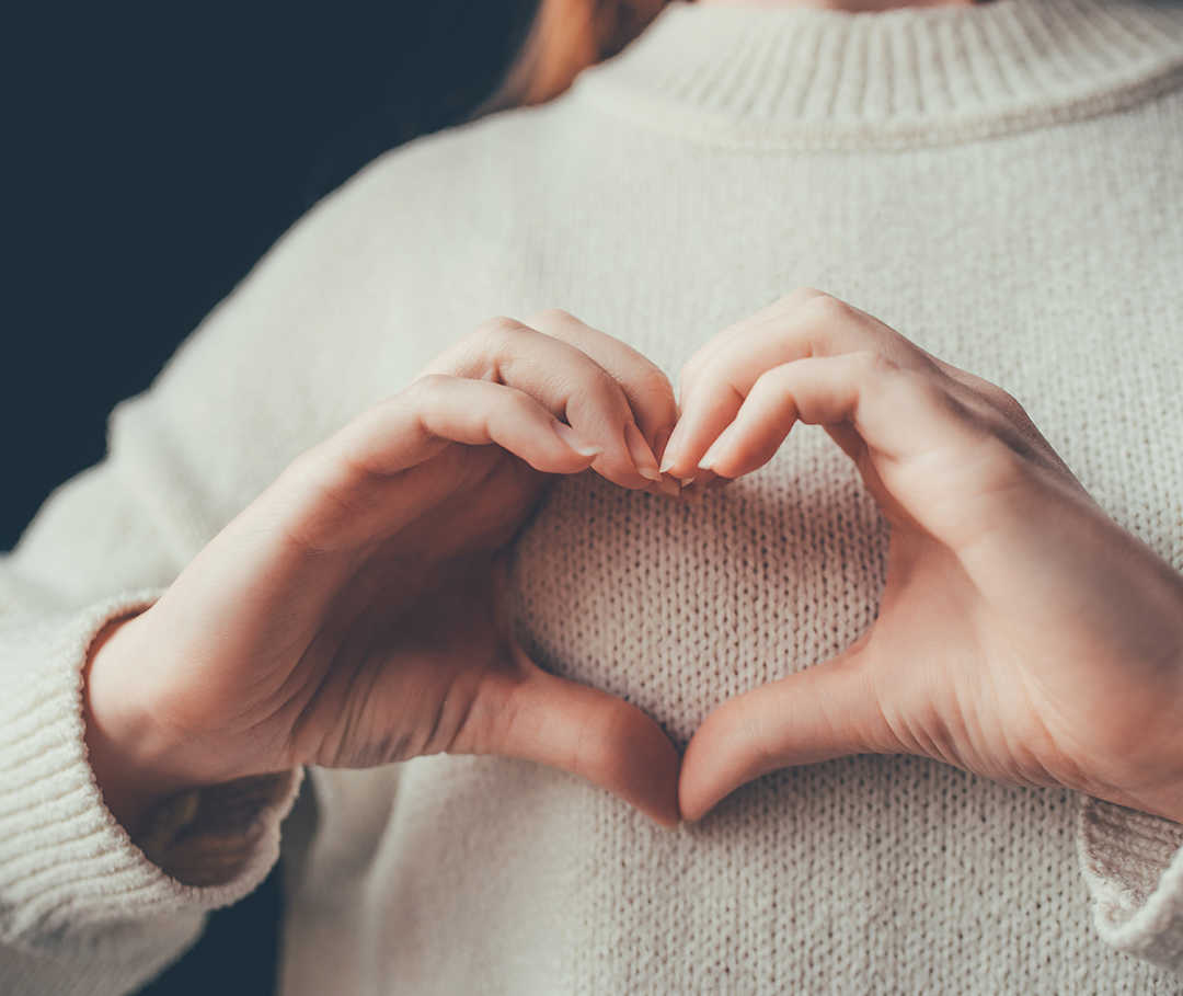 Junge Frau formt mit ihren Händen ein Herz vor ihrer Brust.