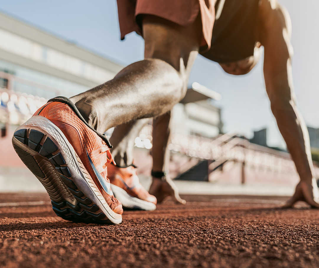 Läufer mit einem Sportlerherz in Startposition auf einer Tartanbahn.