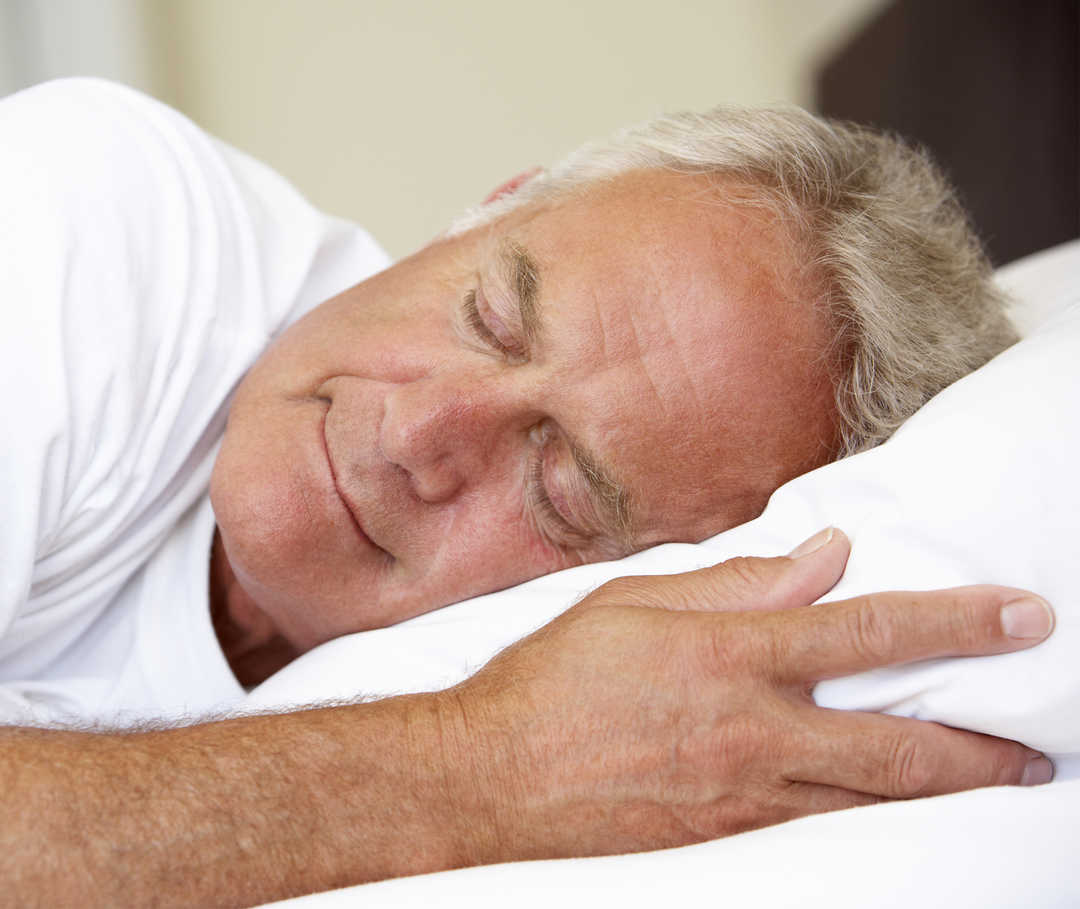 Mann schläft mit erhöhtem Kopfteil im Bett, um Atemnot durch Herzschwäche zu verbessern.